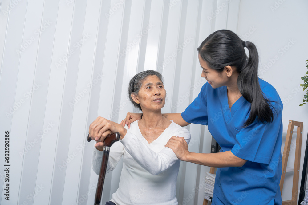 Attentive practitioner nurse assisting physical therapy elderly woman on a walking wood standard cane in disability nursing rehabilitation center, physical therapy encourage hands. Attentive practitioner nurse assisting physical therapy elderly woman on a walking wood standard cane in disability nursing rehabilitation center, physical therapy encourage hands.