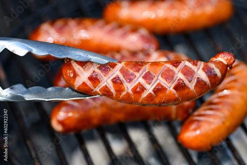 Kiełbasa z grilla nacięta, leżąca na ruszcie, odwracana szczypcami photo