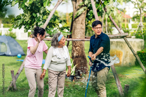 Portrait enjoy happy smiling love multi-generation asian big hug family.Senior mother with young adult woman and son water the tree green plant outdoor in park at home.insurance concept