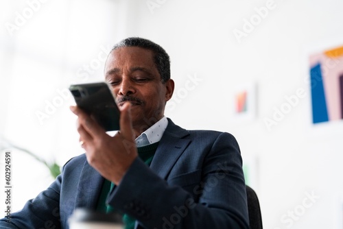 adult Ethiopian male CEO director in formal suit making conversation on mobile phone recording voice message while working in office photo