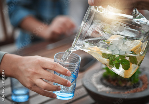 Hands, closeup and water into a glass, outdoor and social gathering with friends, drink and cool down. Zoom, people and friends with clear liquid, ice and lunch with fresh mint, lemon and natural