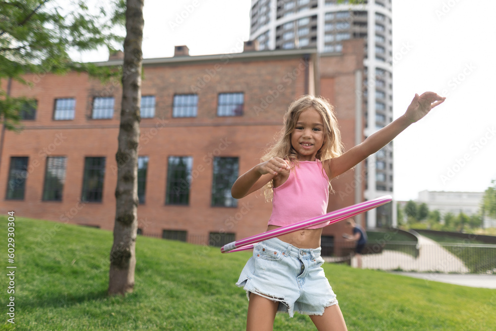 Little girl playing with hula hoop in city park. - obrazy, fototapety, plakaty 