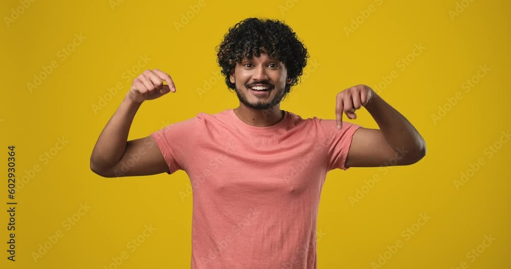 young indian man 20s wear t-shirt point index fingers down on something gesture isolated on orange studio background