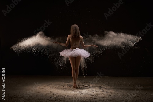 Anonymous female ballet dancer standing on sand in dust clouds