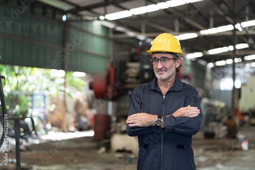 Senior male engineer worker working and standing with crossed arms in factory. Mature male worker with safety uniform, helmet work in industry factory