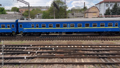 A passenger train travels slowly along the rails, approaching a major railway station in a large city. In the foreground you can see a lot of intertwining rails. Rail transport and passenger