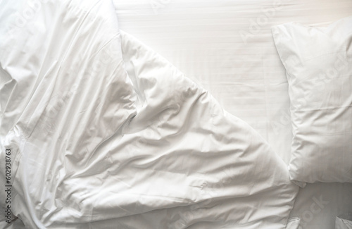 Messy, crumpled bed linen, bedclothes with pillows, sheet and blanket in the morning at a hotel room, top view