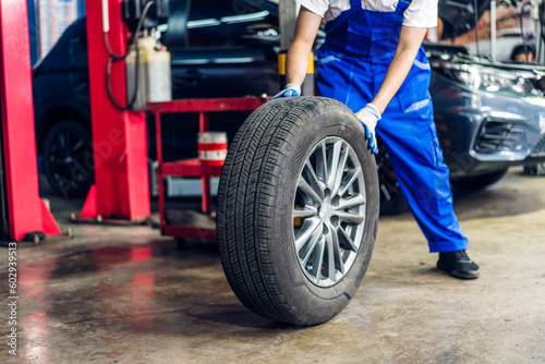 Professional car technician mechanic man in uniform work and maintenance repairing checking removing black wheel tire car before a long travel in auto service.Automobile service garage