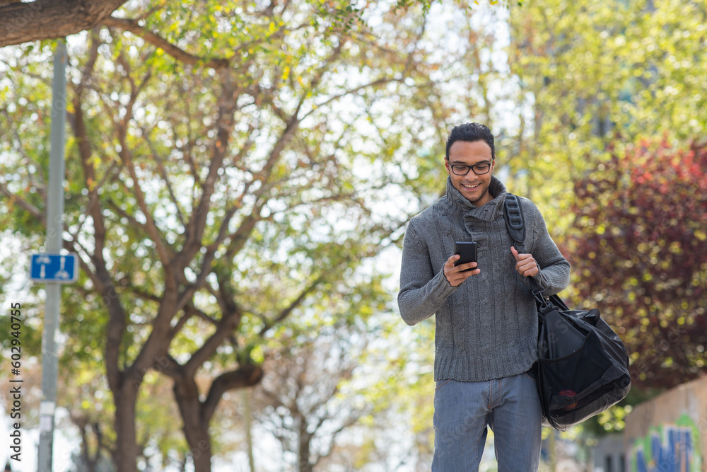 Happy young african american man texting on mobile phone carrying bag outside Happy young african american man texting on mobile phone carrying bag outside