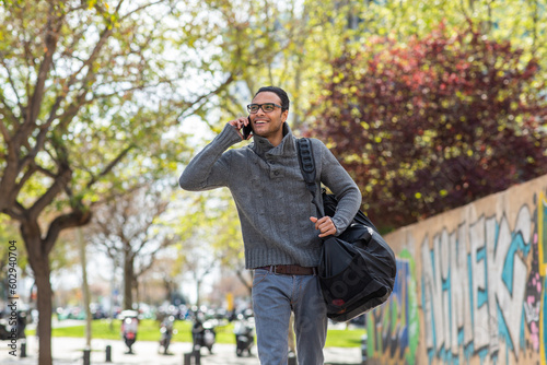 Happy young african american man talking on mobile phone carrying bag outside