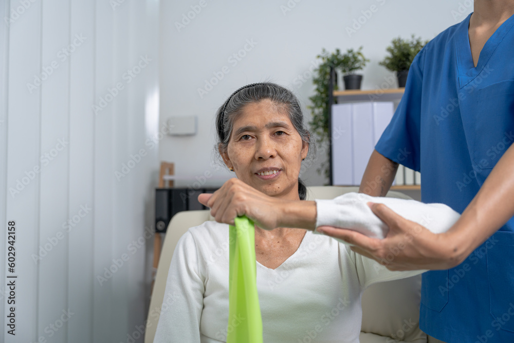 Obraz premium Concept of World Confederation for Physical Therapy. young physiotherapist caregiver helping mature elderly woman training with elastics in rehabilitation center, muscle weakness