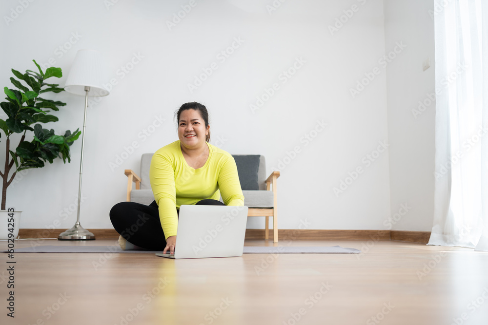 Asian overweight woman doing stretching exercise at home on fitness mat. Home activity training, online fitness class. Stretching training workout on yoga mat at home for good health and body shape. Asian overweight woman doing stretching exercise at home on fitness mat. Home activity training, online fitness class. Stretching training workout on yoga mat at home for good health and body shape.