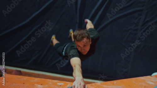 Top-down view, an athlete climber jumps up on a climbing wall indoors and grabs an artificial stone with his hand. Challenging jumps in rock climbing. The climber is hanging on one arm.High quality 4k