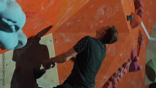 A professional climber trains on a climbing wall in an indoor gym. Performs a difficult jump and grabs an artificial stone on the orange wall of the climbing wall. High quality 4k footage