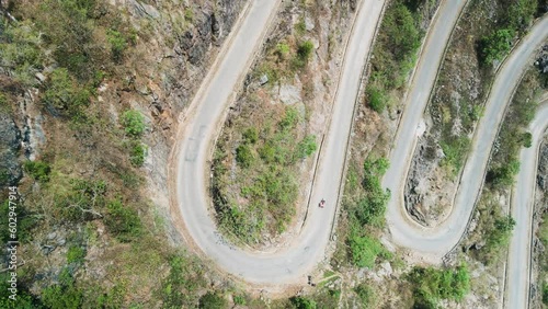 Khau Coc Cha Mountain Pass. Lone vehicle on sharp hair-pin bend. Aerial drone gently rises vertically to reveal series of dramatic, scary bends on steep, twisty mountain road. 