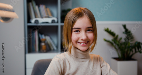 Close up of cute smart caucasian smiling girl loking at camera  indoors. Beautiful girlsitting at table at home with a laptop looks at camera and smiling