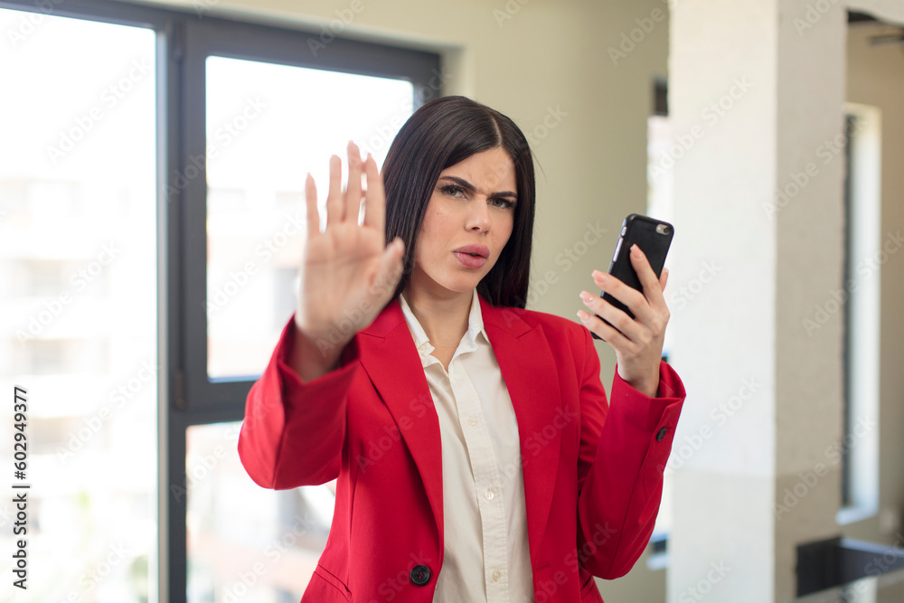 pretty young woman looking serious showing open palm making stop gesture. smartphone concept