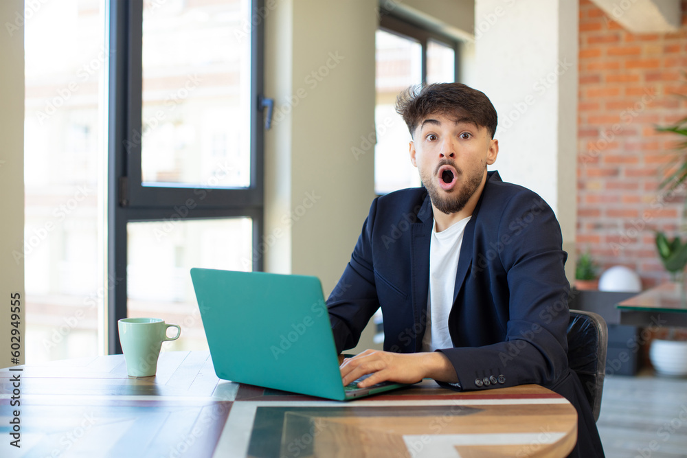 young handsome man feeling extremely shocked and surprised. freelance concept with laptop young handsome man feeling extremely shocked and surprised. freelance concept with laptop