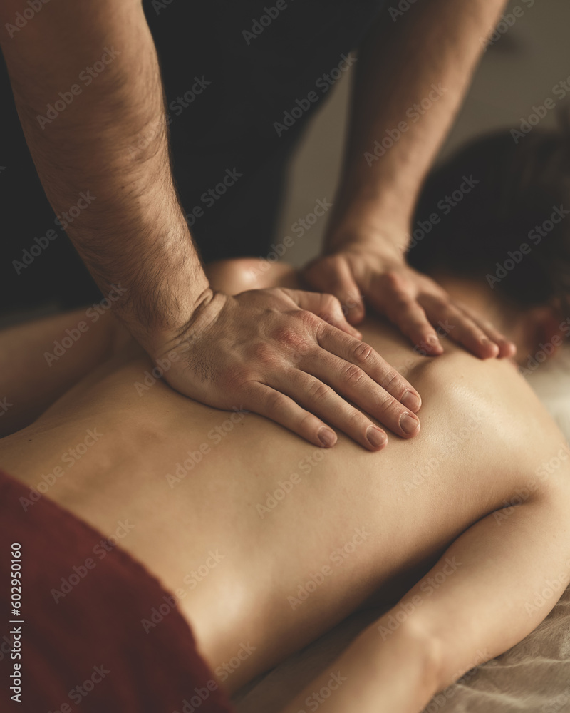 Woman is getting massage. Back massage. Dark-haired woman lies face down on couch. Masseur's hands on back. Relax, spa, body care. View from above. Soft focus.