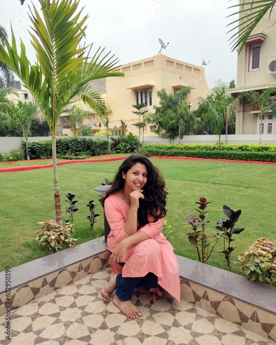 Woman sitting in her home garden in a beautiful evening wearing indian kurti and having a long hair. She is a happy mood and posing camera  photo