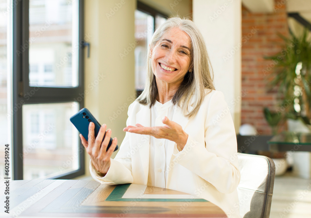 Fototapeta premium pretty senior woman smiling cheerfully, feeling happy and showing a concept with a smartphone