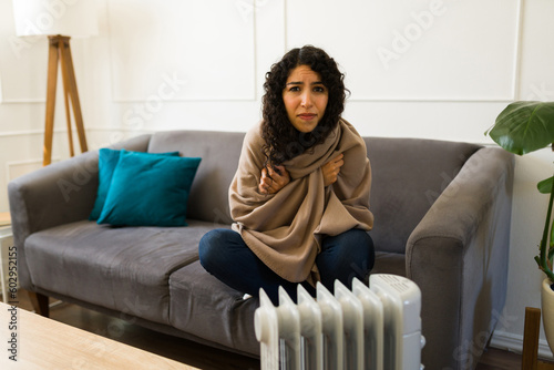 Latin woman shivering from the cold in front of the electric heater