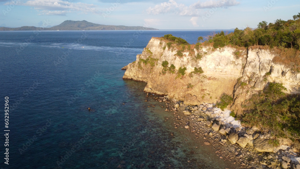 Fototapeta premium Rocky cliff of a tropical island. Aerial view of rocky coastline and blue sea at sunset.