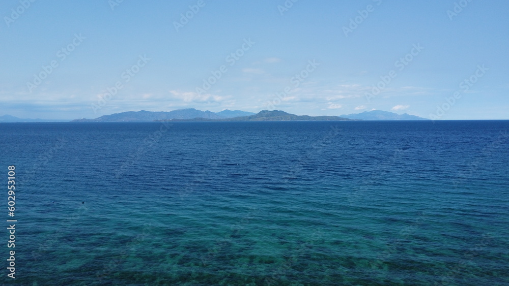 Seascape. Aerial view of the blue sea, white clouds and a tropical island on the horizon.