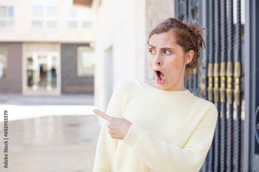 pretty young woman feeling joyful and surprised, smiling with a shocked expression and pointing to the side