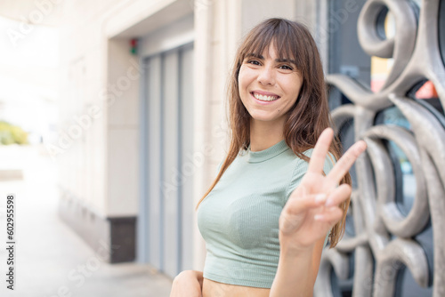 pretty young woman smiling and looking happy, carefree and positive, gesturing victory or peace with one hand Free Download pretty young woman smiling and looking happy, carefree and positive, gesturing victory or peace with one hand - GFXLoad