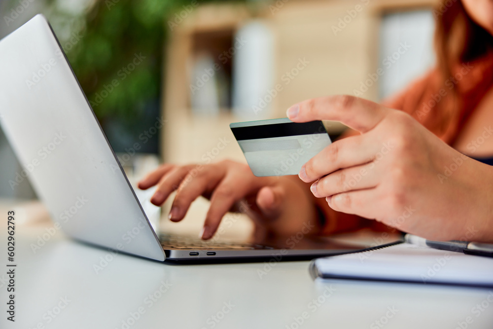 Close-up of a woman holding a credit card and shopping online over a laptop.