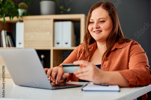 A smiling plus-size woman typing on a laptop, checking a banking account.