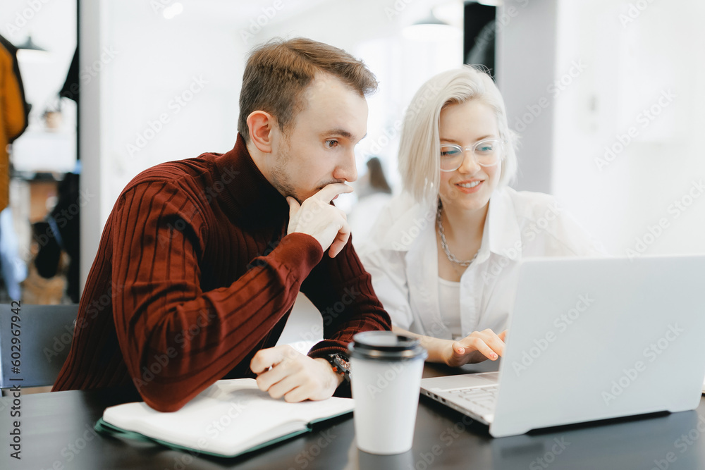 Young IT specialist man discusses startup project with woman designer at laptop in coffee shop. white light Young IT specialist man discusses startup project with woman designer at laptop in coffee shop. white light