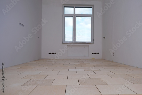 Renovation in a new building. Room with window in perspective. Stage of laying floor. Plywood floor base made of square segments with gaps for expansion. Selective focus