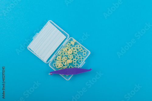 Orthodontic Elastic bands for braces, correcting an overbite. Hook for putting on braces and Ortho wax in plastic box on blue background photo