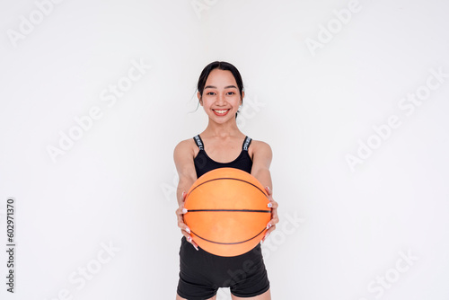 A sporty and athletic young woman posing while holding out a basketball towards the camera with both hands. Isolated on a white background.