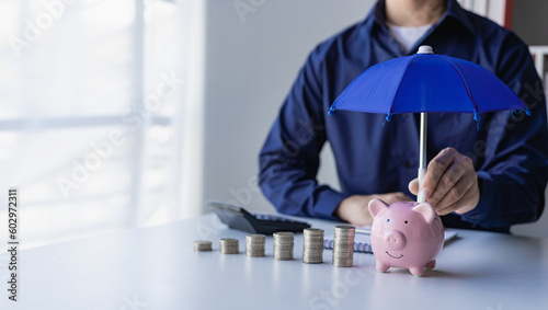 Businessman holding umbrella on pile of money, coins and piggy bank concept Financial insurance and safe investment concept, white background