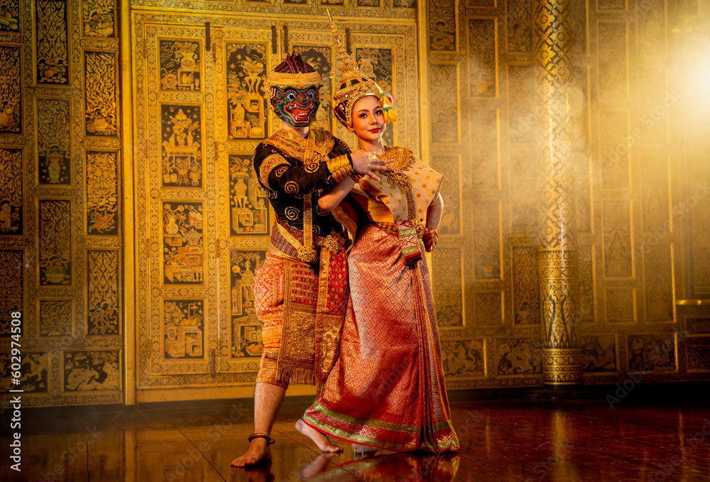 Fototapeta premium Close up beautiful Asian woman wear Thai traditional dress action of dancing together with Thai classic masked from the Ramakien character as black monkey with Thai painting on public place wall.