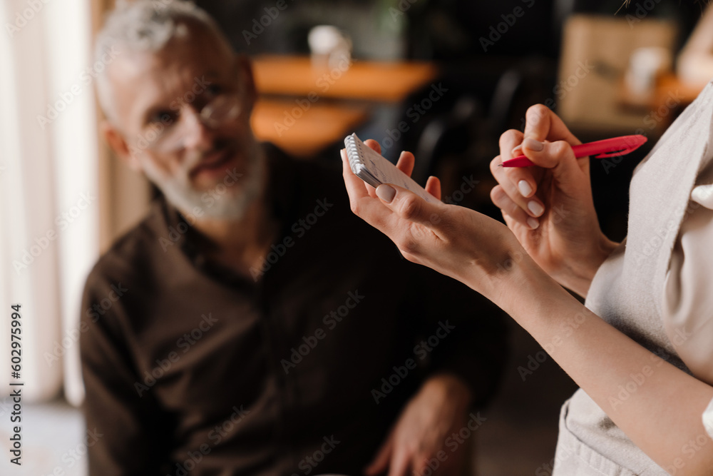 Close-up view of waitress writes down order of elderly man in cafe Close-up view of waitress writes down order of elderly man in cafe