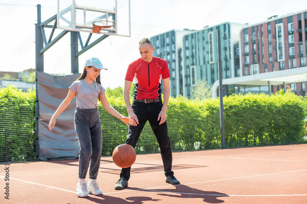 Happy father and teenage daughter playing basketball outside at court