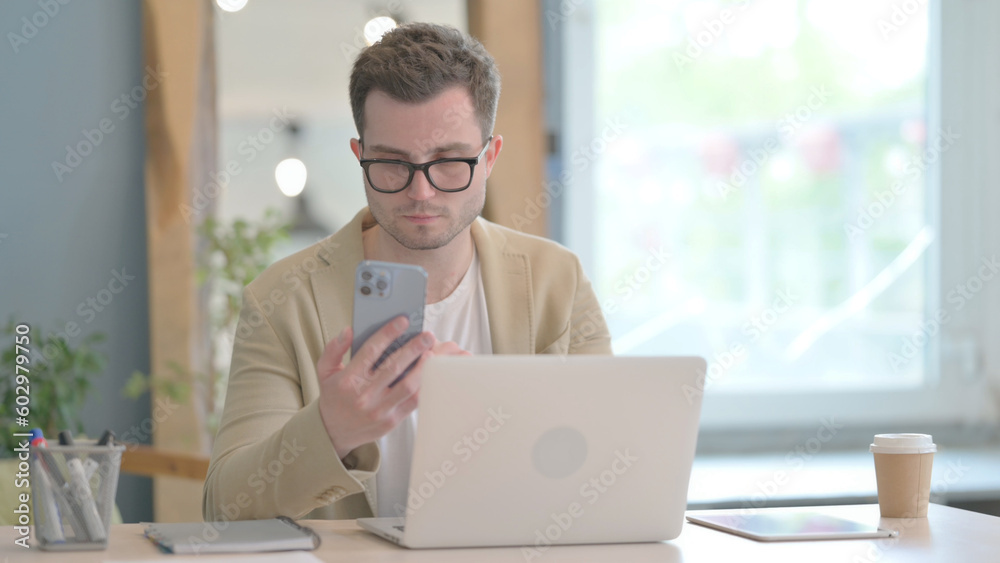 Young Businessman Working on Laptop and Using Smartphone Young Businessman Working on Laptop and Using Smartphone