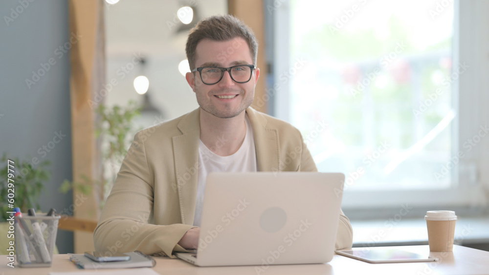 Young Businessman Smiling at Camera while Working on Laptop Young Businessman Smiling at Camera while Working on Laptop