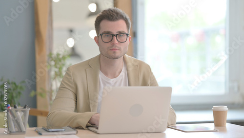 Young Businessman Working on Laptop Looking toward Camera