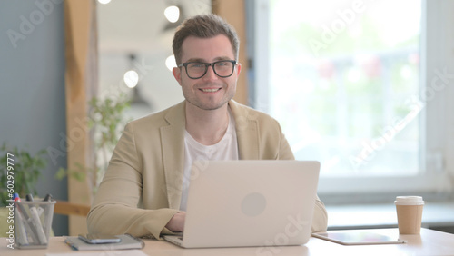 Young Businessman Smiling at Camera while Working on Laptop