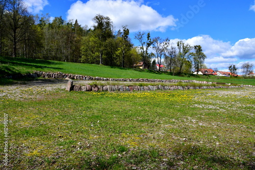 A view of a small valley with a dirt path leading to it, forest and moor everywhere, as well as rock and stone formations scattered around next to lawns or meadows full of flowers and herbs in Poland