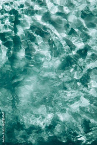 Abstract nature textured background, water waves in the pool with sun reflection, clear green water