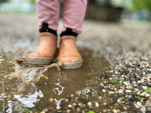 Feet of a child in rubber boots, the child stands in a puddle, splashes water with his feet, walking in the rain © Юлія Антонова
