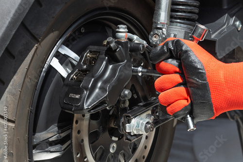 the hand of the master unscrews the bolt of the brake caliper of the electric motorcycle with a wrench, close up