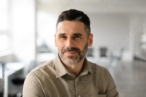 Successful person concept. Portrait of confident bearded middle aged businessman standing in office and posing at camera