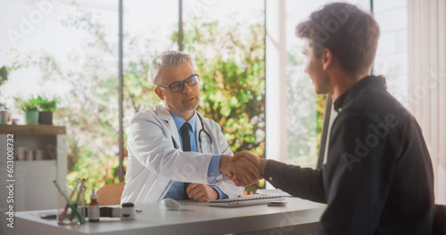 Handsome Middle Aged Doctor is Having a Conversation with a Male Patient, Speaking with Him During Consultation in a Health Clinic. Physician in White Coat Shaking Hands with a Young Man